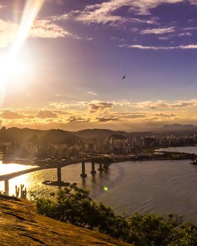 Pôr do sol visto do alto do Morro do Moreno, com a luz dourada sobre a baía, a Terceira Ponte e a cidade ao fundo.